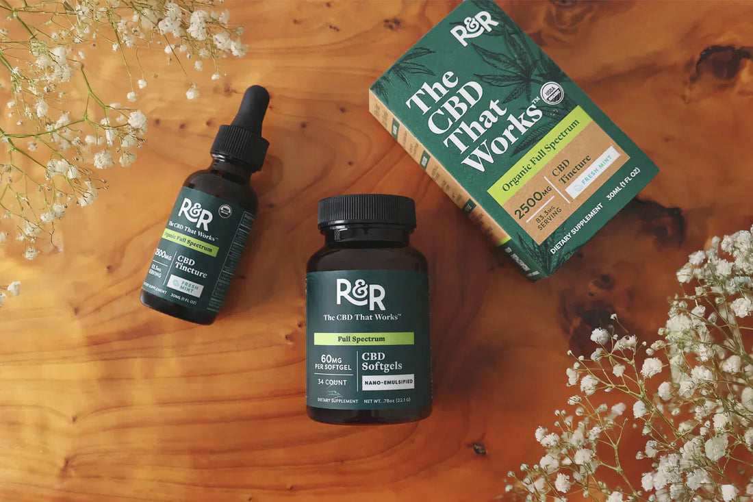 An R&R CBD tincture and a CBD softgels container are placed on a wooden surface