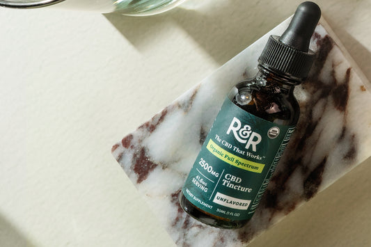 An R&R Organic Full Spectrum CBD tincture placed on a marble stone