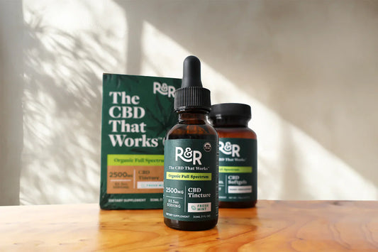 An R&R CBD Tincture and CBD Softgels container placed on a wooden table