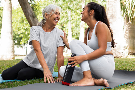 Two ladies are sitting on a mat in the field during yoga, smiling and gossiping