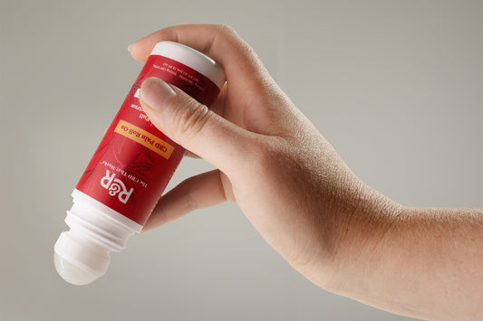 An R&R CBD roll-on held by a man's hand against a gray background